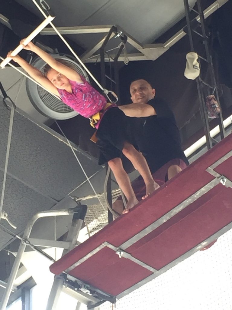 Camper flying on the trapeze with a coach at circus camp